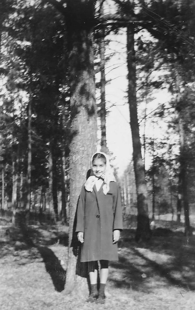 A photo of Sylvia Bracklin as a young girl in a coat and headscarf in the woods. Photo courtesy of Sylvia Bracklin-Baker.